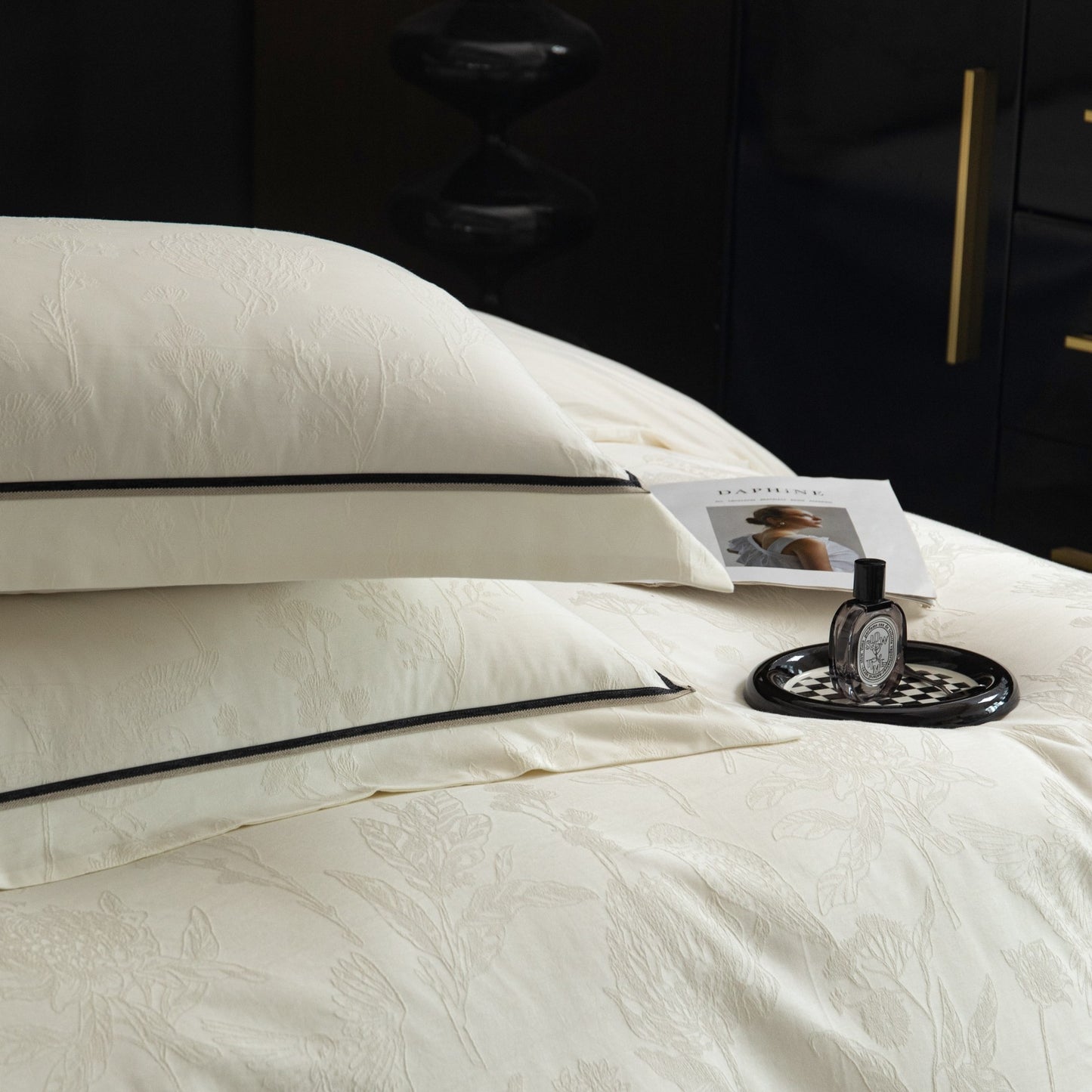 Ivory sateen bedding set with subtle floral pattern and black trim, featuring duvet cover and pillowcases on a bed.