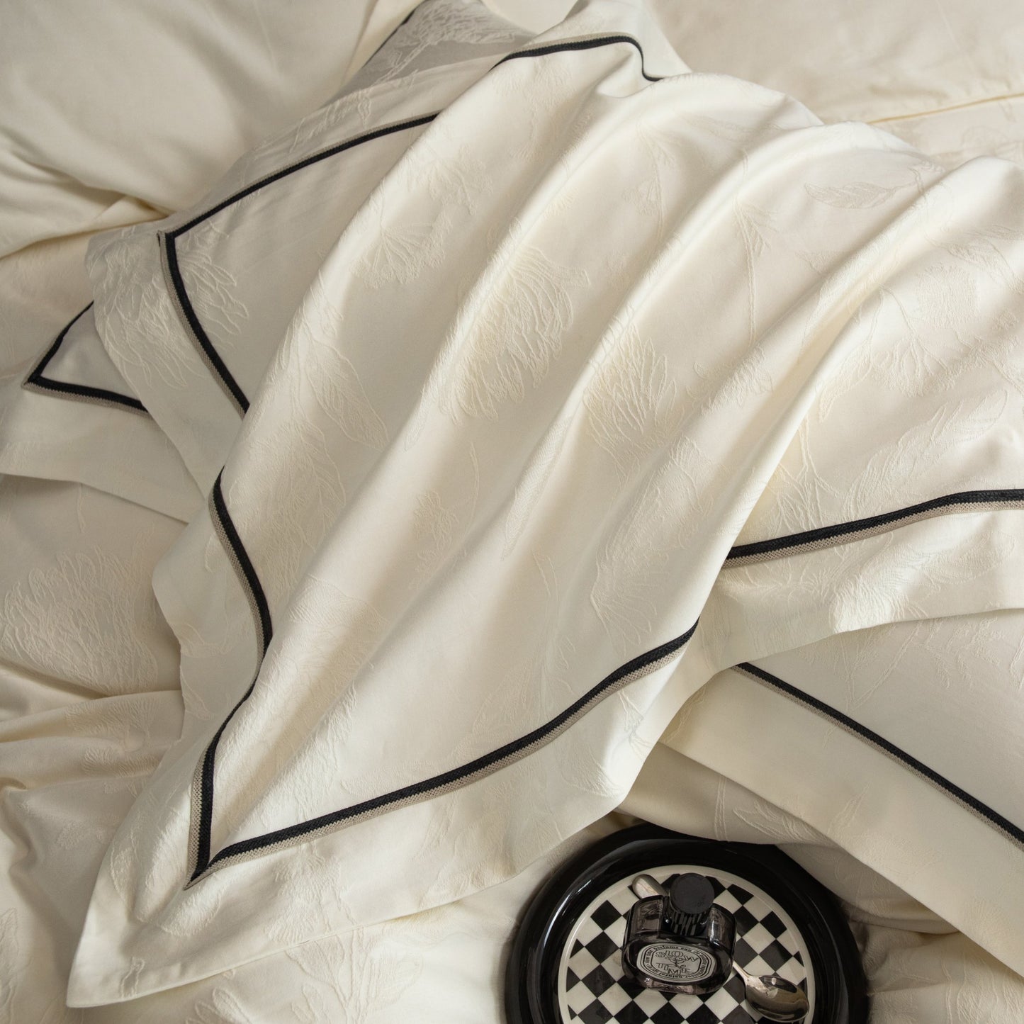 Close-up of luxurious white sateen bedding with black trim from the Paris collection featuring intricate patterns and silky texture.