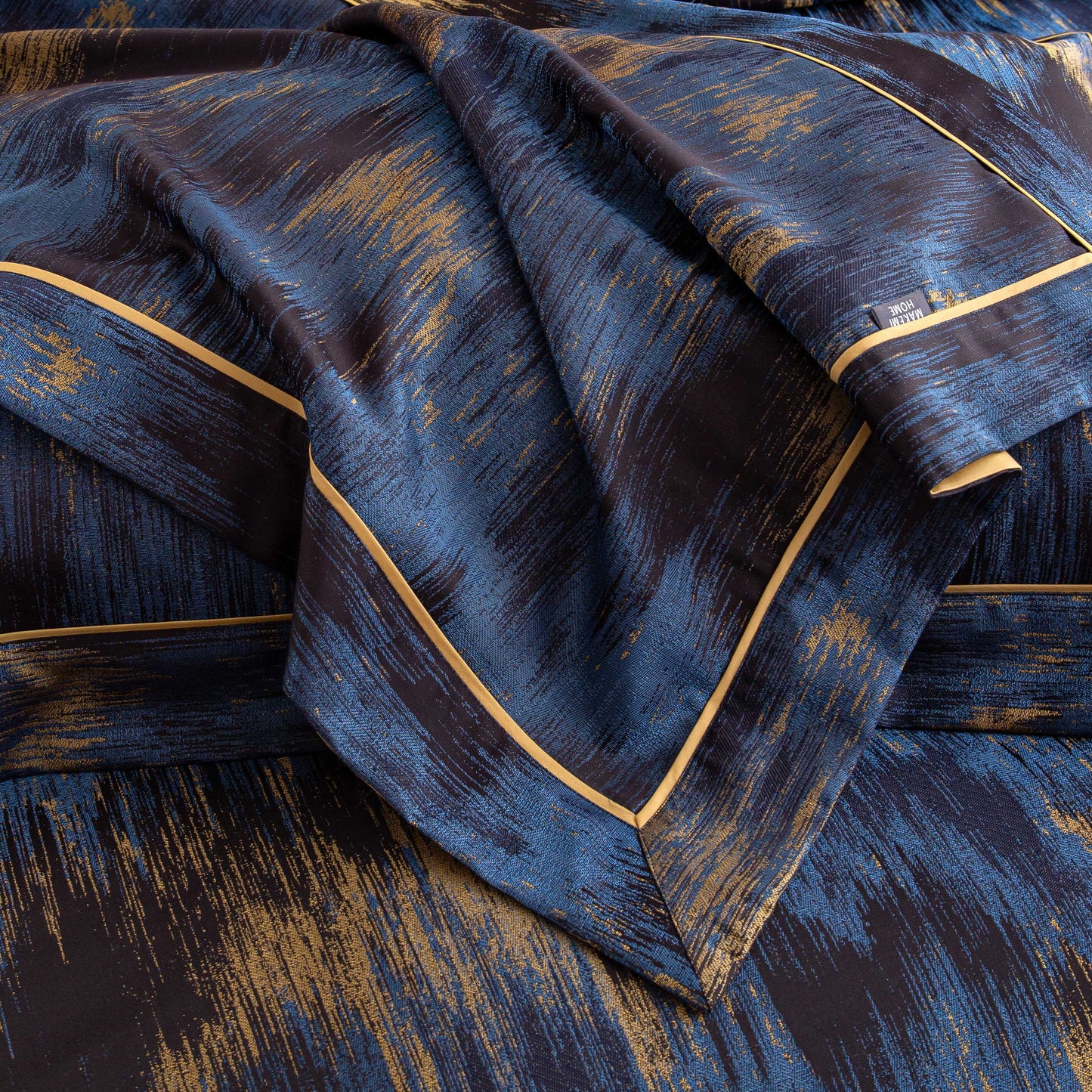 Close-up of Marrakech sateen bedding set in deep blue and gold tones with silky smooth texture and elegant design.