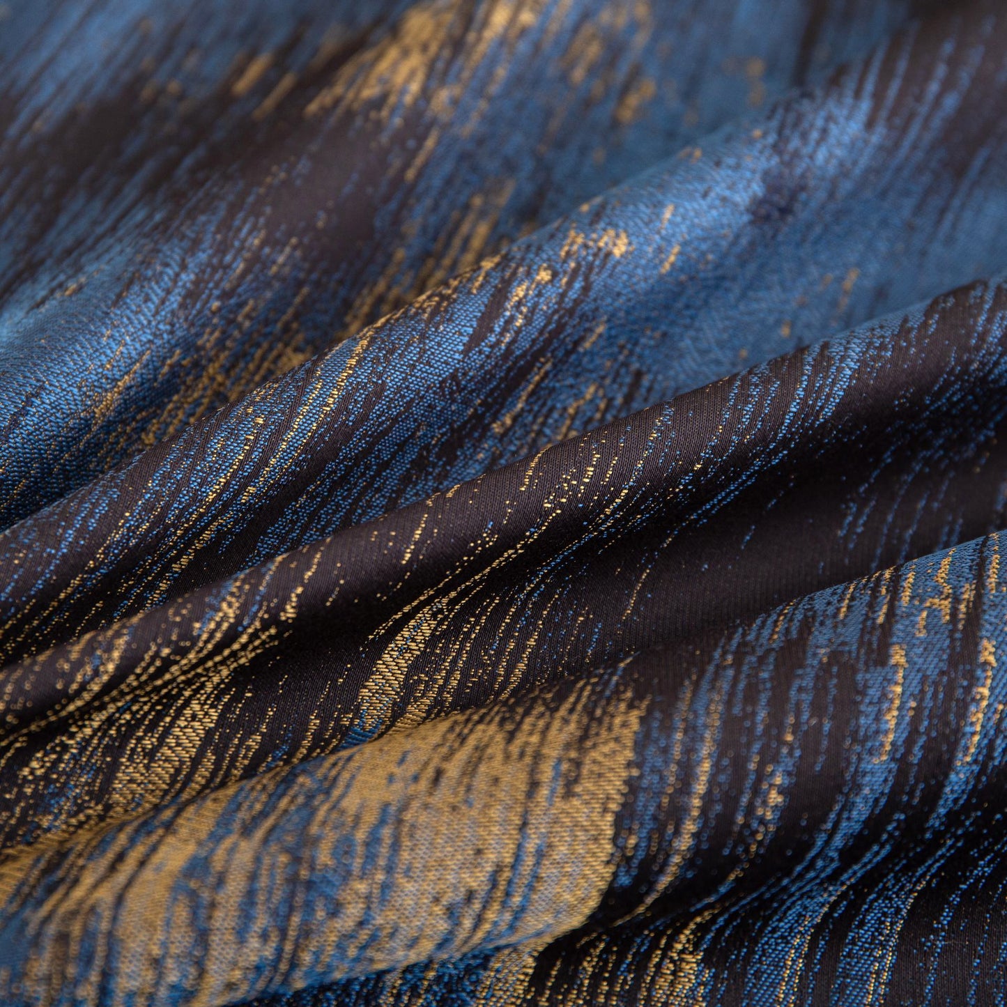 Close-up of luxurious Marrakech sateen bedding fabric in rich blue and gold tones with silky smooth texture and elegant pattern.