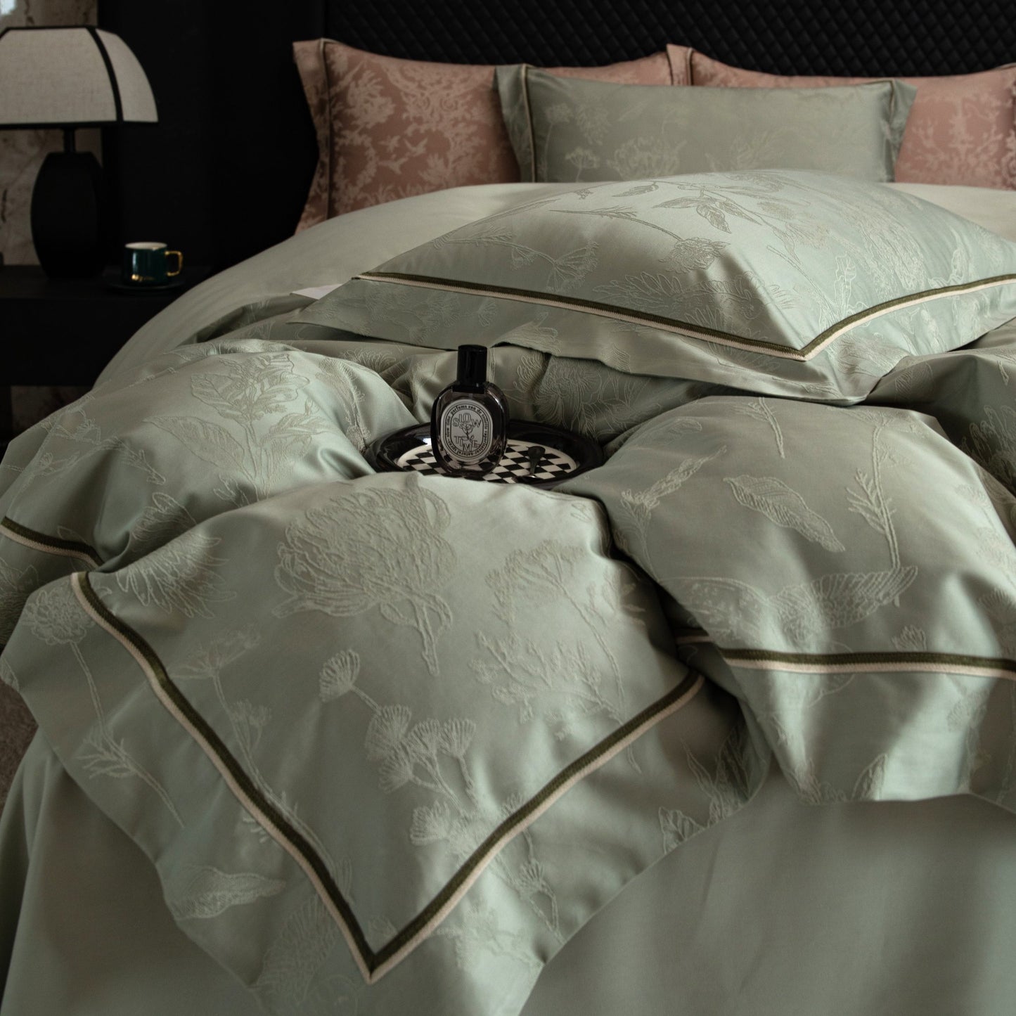 Luxurious Avignon sateen bedding set in soft green with floral embroidery and contrast piping on a modern bed.