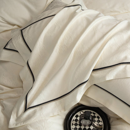 Close-up of luxurious white sateen bedding with black trim from the Paris collection featuring intricate patterns and silky texture.