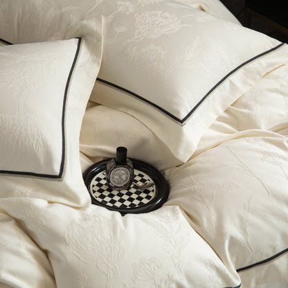 Cream sateen bedding set with subtle floral patterns and black trim, styled with a small decorative tray and bottle.