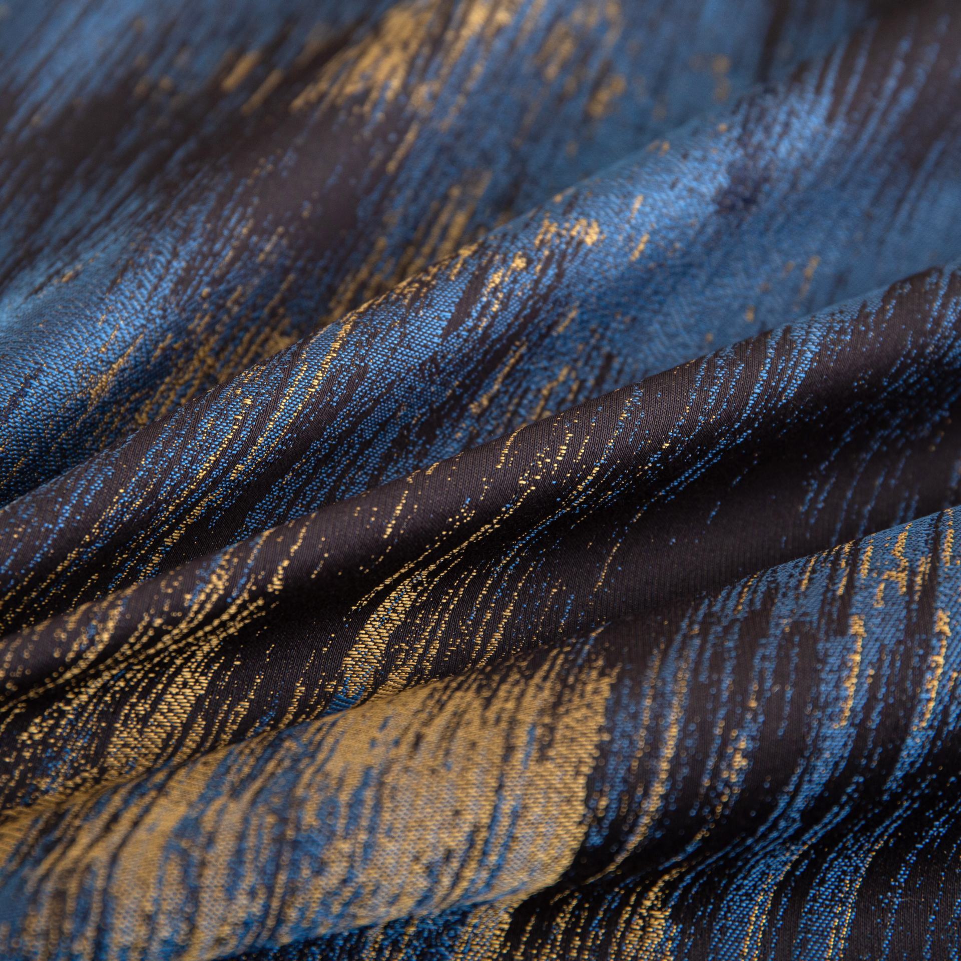 Close-up of luxurious Marrakech sateen bedding fabric in rich blue and gold tones with silky smooth texture and elegant pattern.